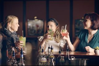 A stylish outdoor bar features a unique umbrella structure with hanging lights, surrounded by greenery and modern seating.