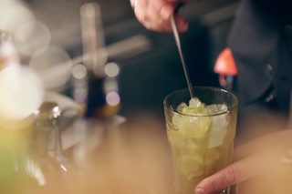 A hand holds a glass of white wine while another holds a pint of beer, accompanied by tacos and chips on a wooden table.