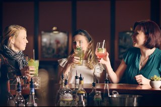 A stylish outdoor lounge features comfy seating, palm trees, and ocean views, enhanced by string lights and a large umbrella.