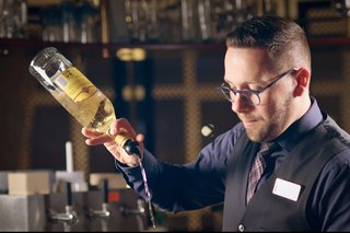 A couple shares a joyful moment at a bar, holding cocktails and smiling, with palm trees and a vibrant sky in the background.