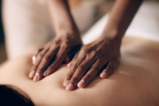 A person and a child in matching robes and towel headdresses stand on a balcony, gazing at the serene ocean and beach view.
