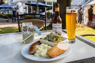 A couple enjoys drinks on a sunny lounge, laughing together amidst a vibrant beachside setting with palm trees in the background.