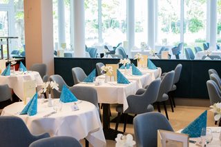 A vibrant restaurant with modern decor, featuring yellow chairs, wooden tables, and large windows offering a view of palm trees and the ocean.