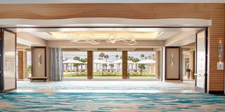 A spacious, elegant entryway leads to a serene outdoor area with palm trees and umbrellas, complemented by modern decor and vibrant flooring.