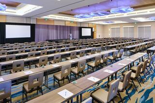 A spacious conference room is set up with rows of tables and chairs, featuring screens at the front, ready for an event.