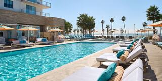 A luxurious pool area with lounge chairs, bright umbrellas, and palm trees, set against a sunny sky and ocean view. Perfect for relaxation!