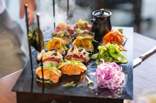 A vibrant plate features colorful citrus slices and green pesto atop crusty bread, garnished with microgreens and drizzled with oil.