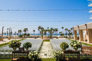 A serene outdoor wedding setup with rows of white chairs, lush floral arrangements, and a stunning ocean backdrop under clear blue skies.