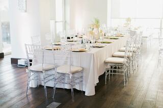 A elegantly set dining table with clear chiavari chairs, adorned with gold accents, ready for a sophisticated gathering.