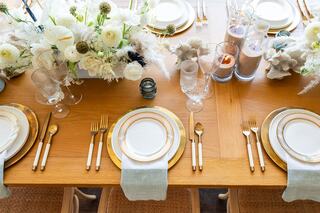A beautifully arranged dining table featuring elegant plates, golden cutlery, and a bouquet of white flowers for a sophisticated setting.