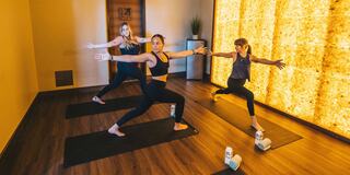 Three women practice yoga in a peaceful studio, focusing on their poses amidst a warm, inviting atmosphere with soft lighting.