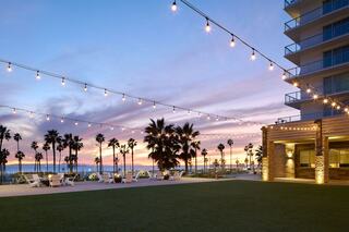 A serene beachfront scene features palm trees, lounge chairs, and string lights against a colorful sunset sky, evoking tranquility and relaxation.