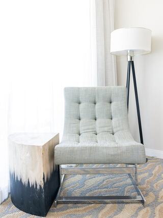 A modern gray armchair with tufted upholstery sits beside a unique wood side table, complemented by a sleek floor lamp in a bright, minimalist space.