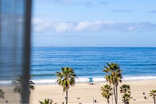 A serene beach scene with gentle waves, distant ships, and palm trees swaying under a clear blue sky. Perfect coastal tranquility.