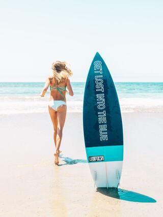 A woman carrying a surfboard runs through the shallow waves at the beach on a sunny day.
