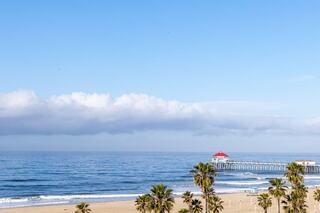 A serene beach scene features gentle waves lapping at the shore, palm trees swaying, and a distant pier under a clear blue sky.