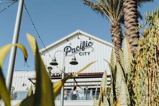 A building sign reads "Ostsee City," with palm trees and outdoor seating visible, creating a vibrant, sunny atmosphere.
